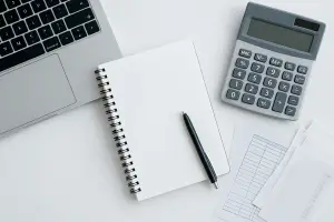 Heller Schreibtisch mit Laptop, Taschenrechner, Notizbuch und Stift – symbolisch für Buchhaltung, Finanzen und Unternehmensberatung im WohnMeta-Stil